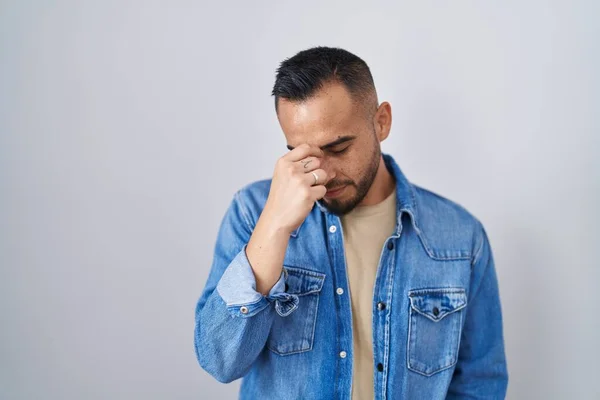 Young hispanic man standing over isolated background tired rubbing nose and eyes feeling fatigue and headache. stress and frustration concept. 